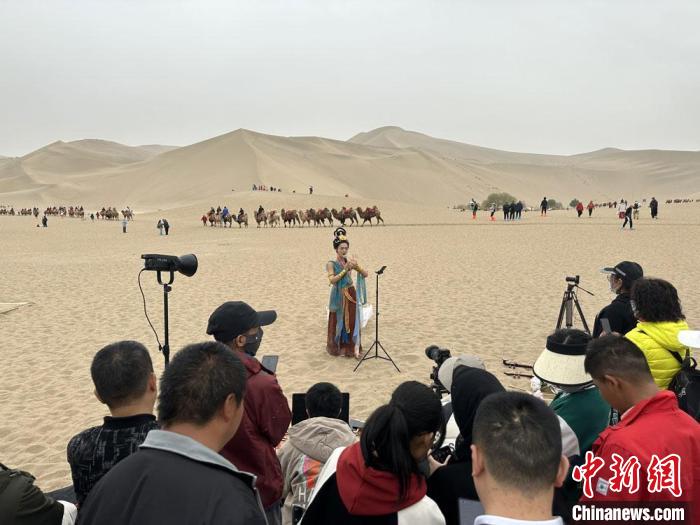 圖為2023年4月底，敦煌大漠“逐舞者”奧楠在鳴沙山月牙泉景區(qū)視頻直播，吸引游人圍觀?！●T志軍 攝