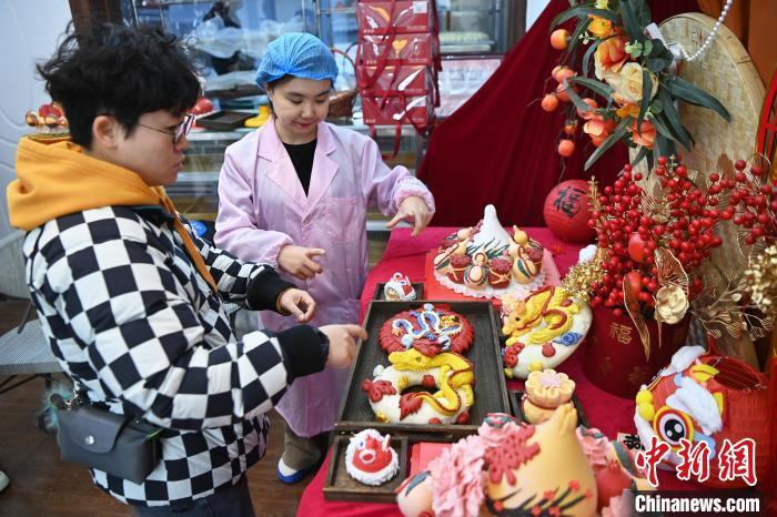 1月25日，隨著春節(jié)臨近，蘭州一花饃店“龍”元素花饃熱銷。圖為工作人員向顧客推薦“龍”元素花饃。九美旦增 攝</p><p>